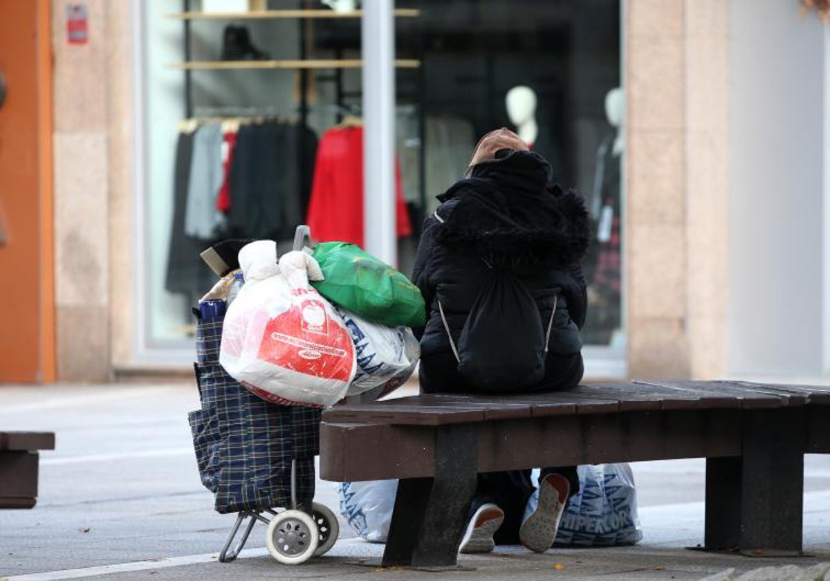 Una mujer sin recursos, descansa en un banco con todas sus posesiones en un carrito y en bolsas.