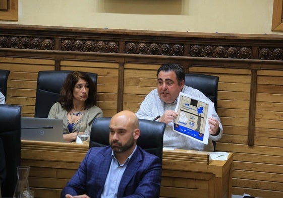El edil de Tráfico, Pelayo Barcia, muestra durante el Pleno un cartel publicitario del Principado para promocionar la tarjeta Conecta en Gijón.