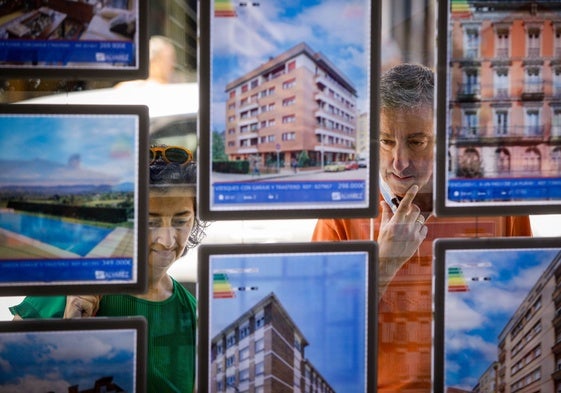 Dos personas consultan las ofertas de una agencia inmobiliaria en Gijón.