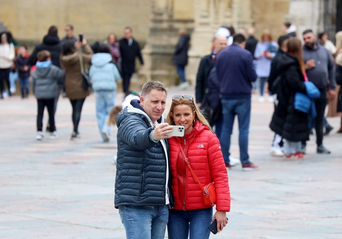Una pareja se hace una foto en Oviedo con la catedral de fondo.