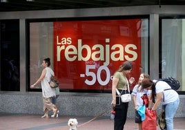 Personas, delanta de un cartel de rebajas, del centro de Oviedo.