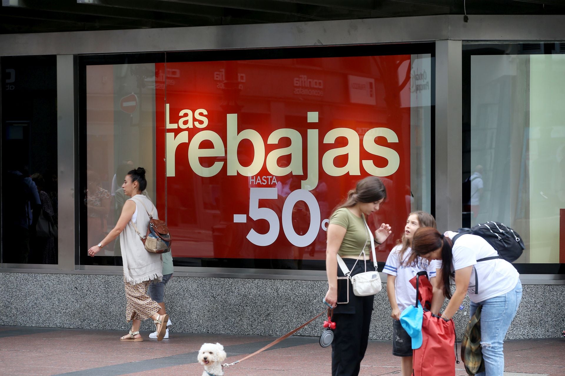 Personas, delanta de un cartel de rebajas, del centro de Oviedo.