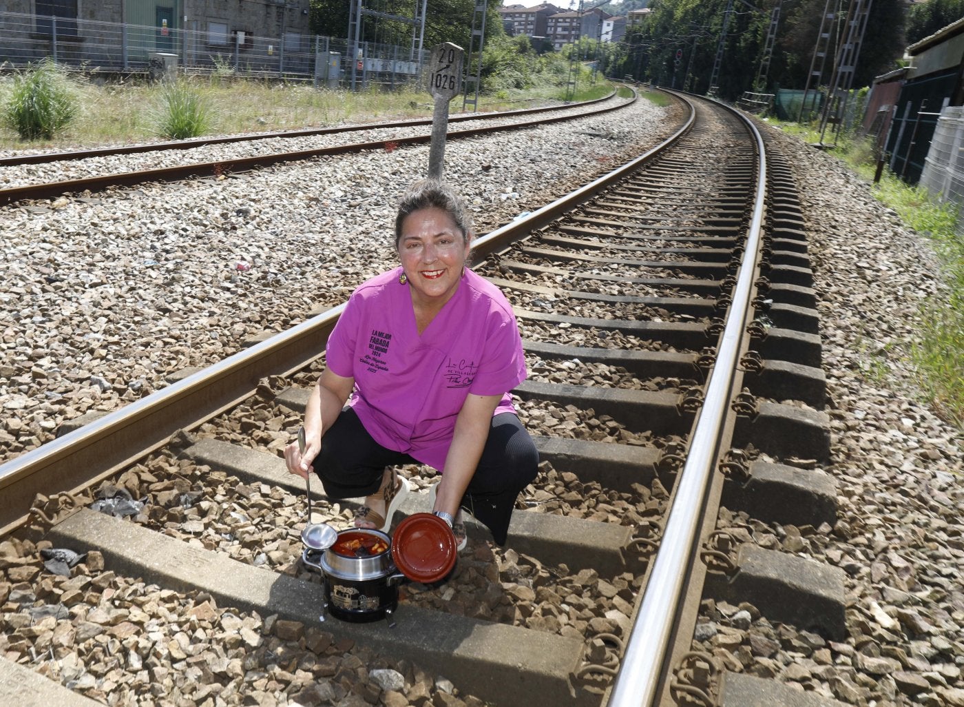 Pilar Meana, con una fabada en su olla ferroviaria, posa en las vías del tren junto a su negocio.