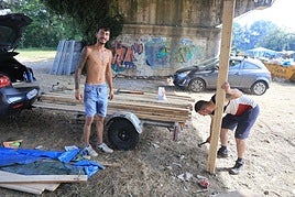 Dos jóvenes retiran tablones de madera y los colocan en su remolque.