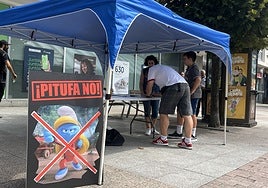 Al fondo, vecinos firmando en el puesto del PP, presidido por un cartel contra la figura de la pitufa, junto a la plaza cubierta.