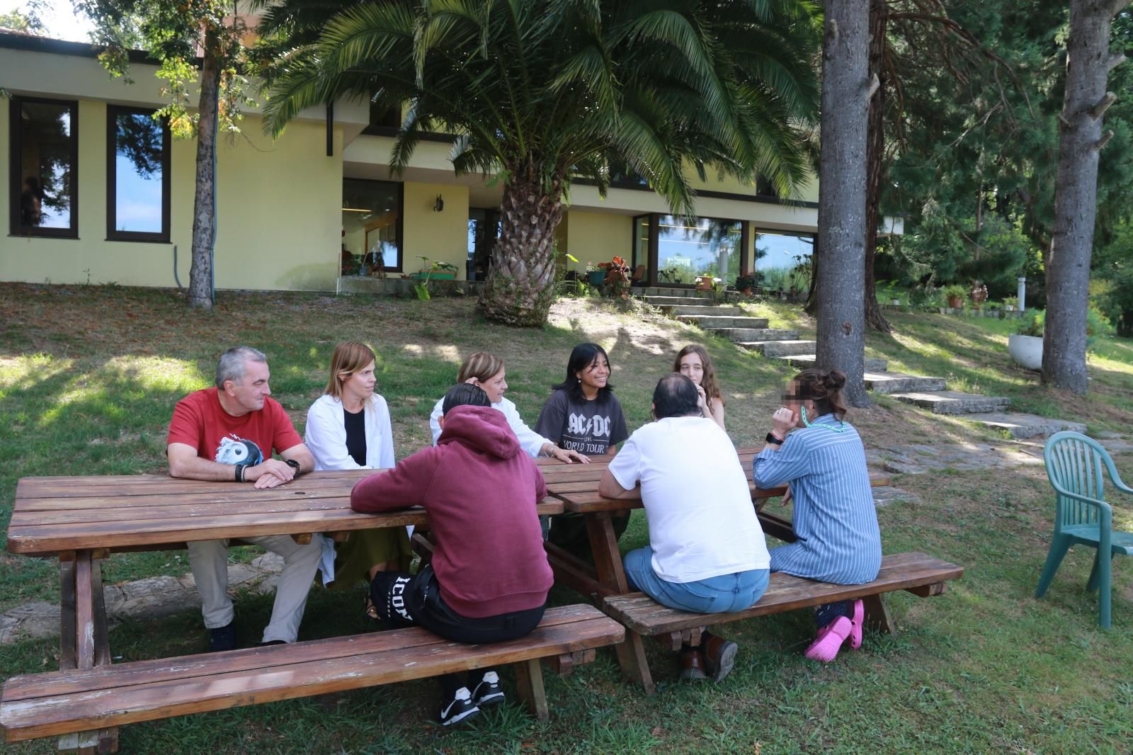 Jesús González, la psicóloga Paula Pérez, la educadora Victoria Canelo y las voluntarias de Cáritas Sherly Roxana Caiza y Lorena Fernández, con varios pacientes en una de las mesas del jardín de La Santina.