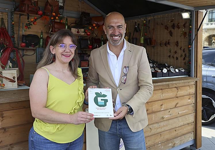 Sonia Fernández, de Ventolín Artesanía, recoge el diploma 'Al puestu más prestoso' entregado por Óliver Suárez (Divertia).