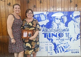 Noemí García y Ana Fernández posan muy sorientes con el mural de azulejos azules y la fotografía de los fundadores, Tino y Maruja, en el restaurante ubicado en la calle Alfredo Truán.
