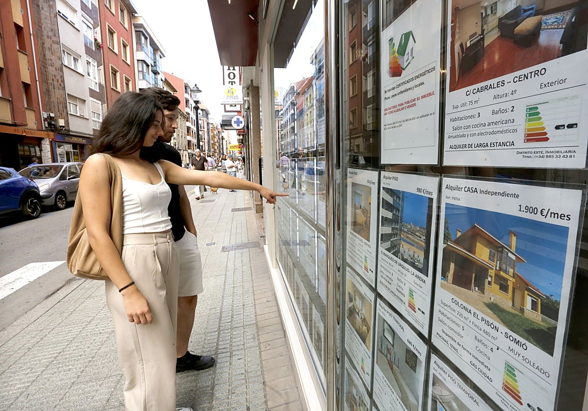 Dos jóvenes consultan las ofertas de una inmobiliaria de Gijón.
