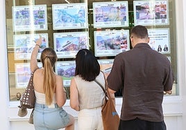 Varias personas observan los anuncios de pisos en venta en una inmobiliaria ovetense.