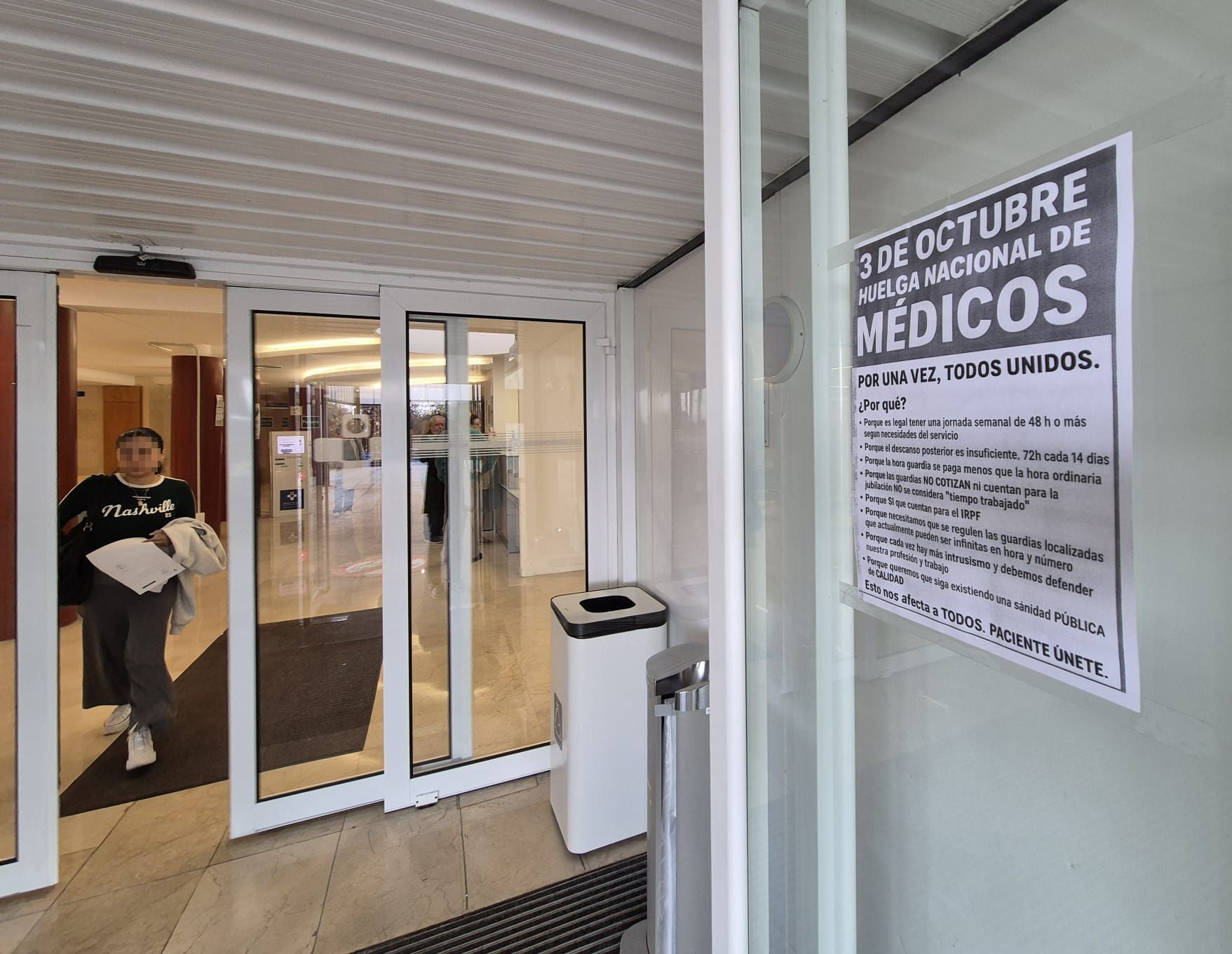 Una paciente sale de un centro de salud de Gijón, en cuya entrada se puede leer un cartel que recoge los principales motivos de la huelga nacional de médicos.