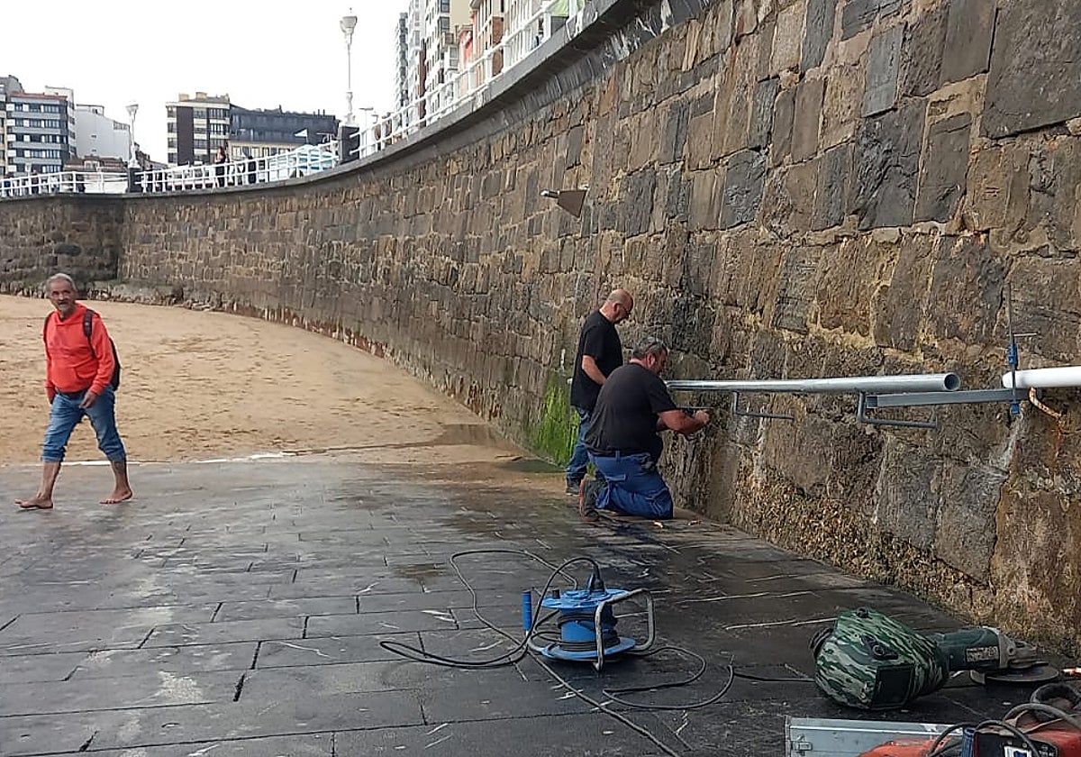 Dos operarios, en plena labor para colocar el nuevo tramo de barandilla en la Rampla de la playa de San Lorenzo, de Gijón.