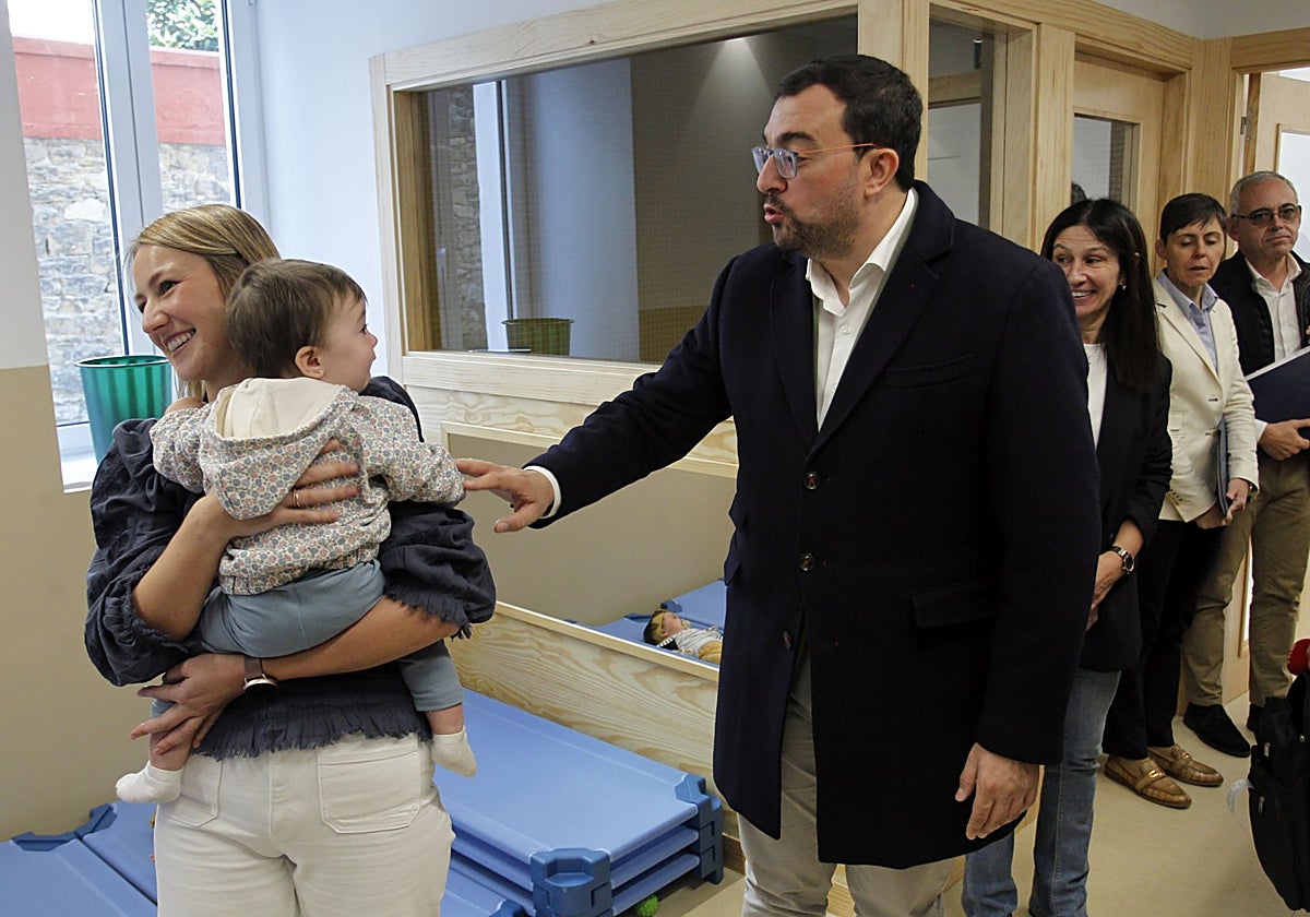María Acera, con un bebé en brazos, durante la visita el presidente regional, Adrián Barbón, y otros responsables regionales y locales, a la sede de la escuelina en San Lázaro.