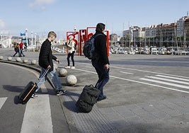 Una pareja cruza con sus maletas hacia los gijoneses Jardines de la Reina.