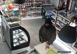 El atracador amenaza con el arma a un empleado para que deje el móvil en el mostrador.