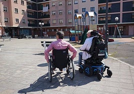 Dos personas pasean con ayuda de su silla de ruedas.