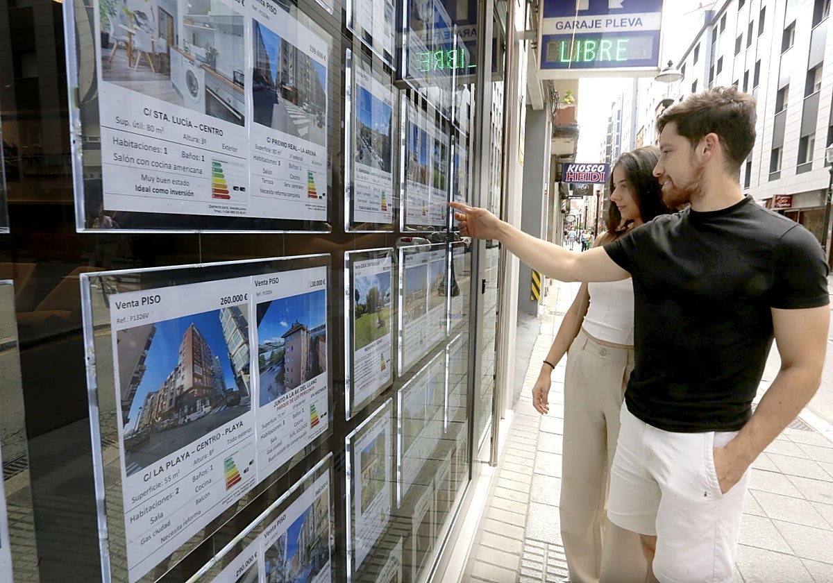 Dos jóvenes observan los precios de la vivienda en una inmobiliaria de Gijón.