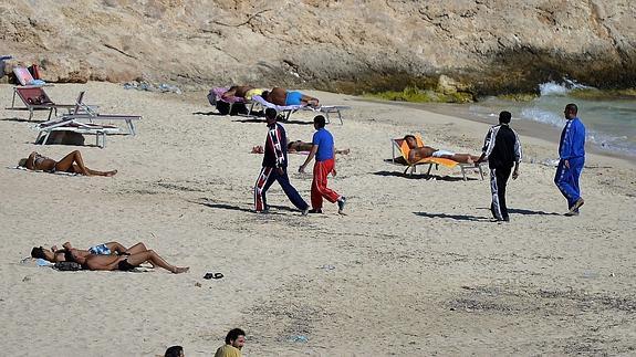 Varios inmigrantes llegados a la costa de Lampedusa caminan por la playa. Archivo