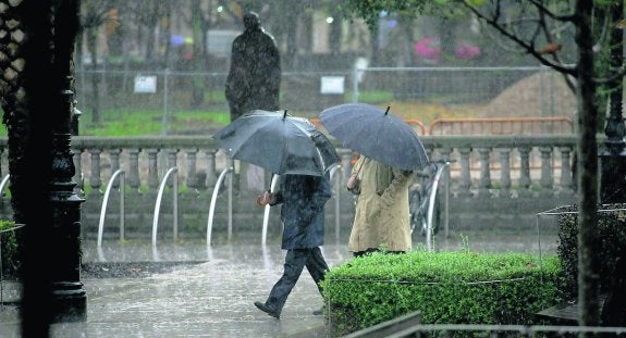 Dos personas caminan por el paseo de Begoña protegidos de la lluvia con sendos paraguas. 