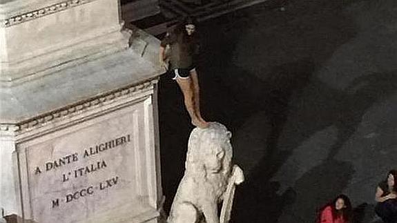 La turista subida uno de a uno de los cuatro leones de la escultura de Dante Alighieri.