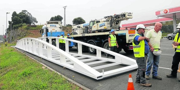 Operarios de la empresa Grúas Roxu tras depositar en el aparcamiento de la gasolinera de Posada parte de la estructura de la pasarela peatonal de Llanes. 