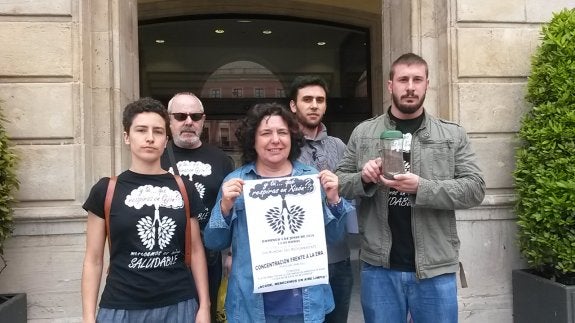 Los vecinos, con el cartel de la concentración del domingo contra la contaminación del aire y un tarro con partículas recogidas en dos días en una terraza de Veriña. 