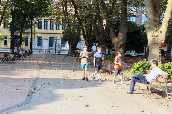 Varios niños, en el parque y, detrás, muchas hojas secas. 