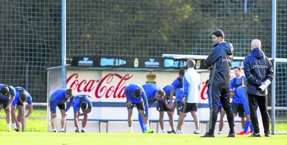 Fernando Hierro, en primer término, pensativo junto a su ayudante Julián Calero, mientras sus futbolistas realizan ejercicios de estiramiento sobre el césped de las instalaciones de El Requexón.