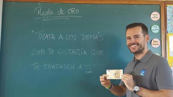 Carlos Llaca, con el billete y en la pizarra una regla de oro que tienen en su clase.