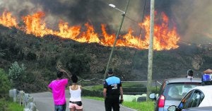 Una agente de la Policía Local de Avilés y una pareja observan las llamas en la zona alta de la carretera que une La Folleca, en San Cristóbal, con Raíces Nuevo ::                             SERGIO LÓPEZ