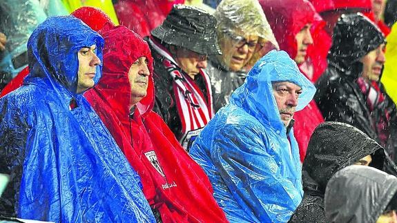 Aficionados se protegen de la lluvia durante un partido en San Mamés.