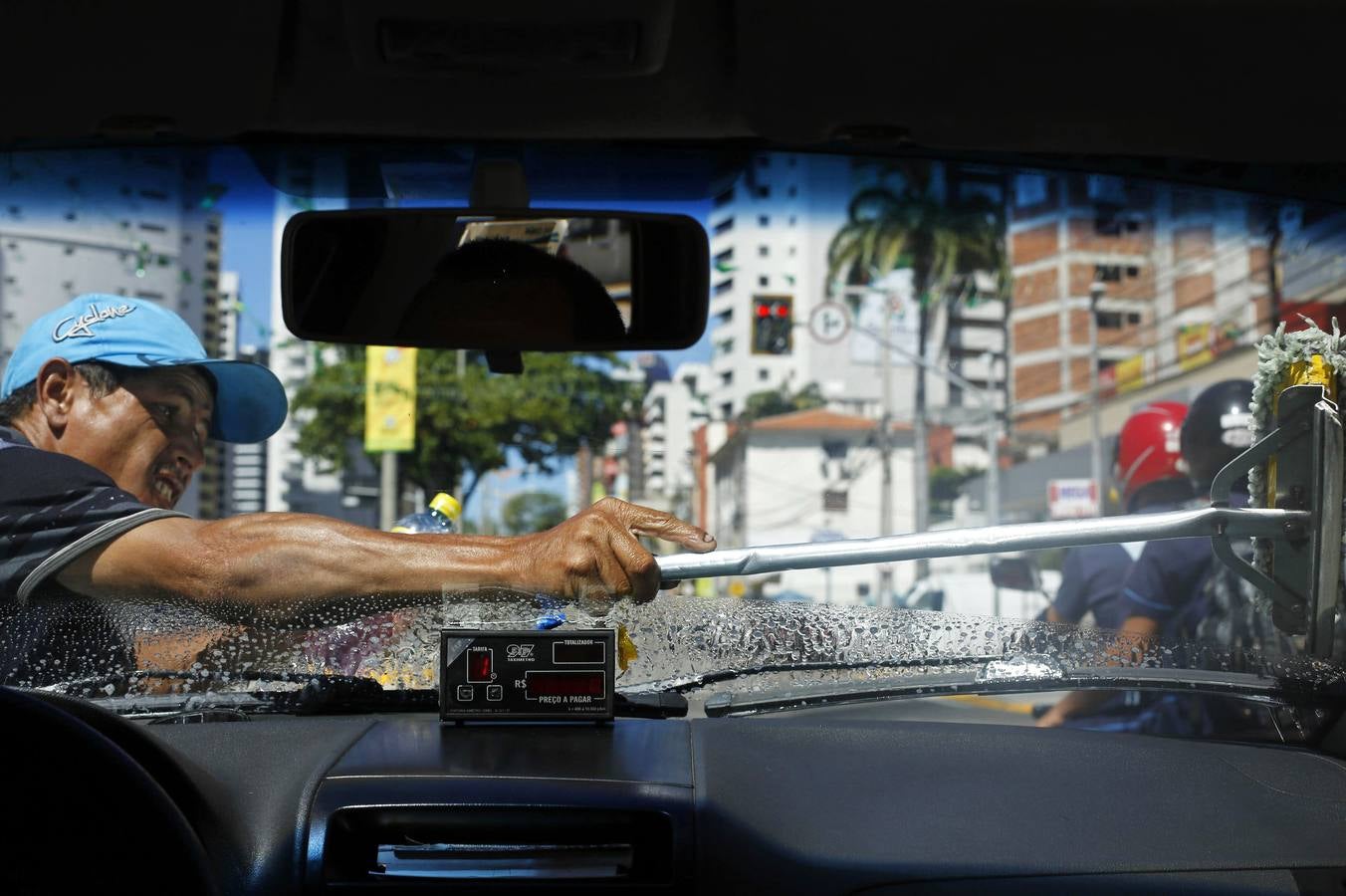 Un hombre limpia el parabrisas de un taxi a cambio de dinero mientras espera que cambie el semáforo en una calle de Fortaleza