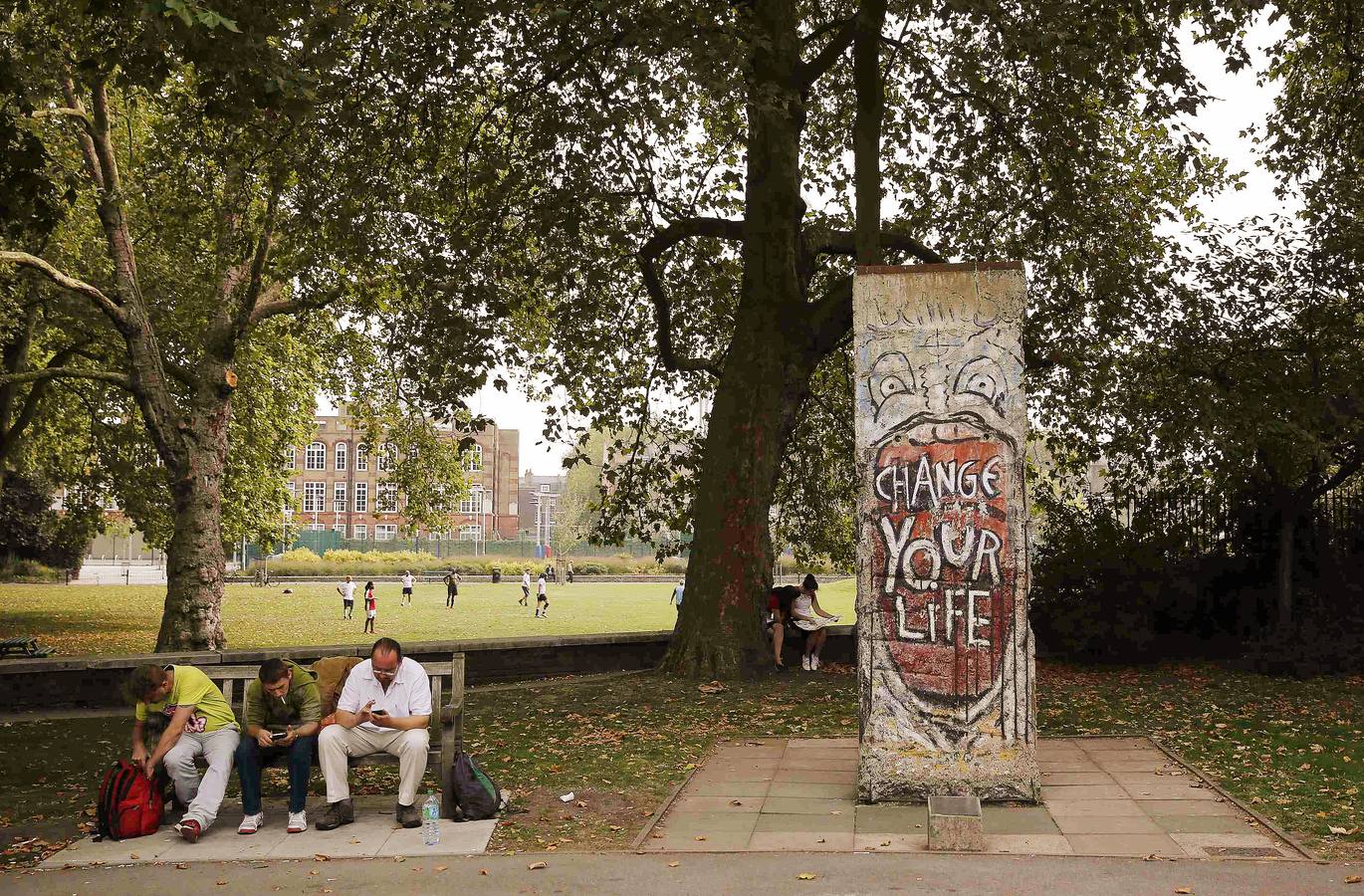 Varios hombres sentados en un banco, junto al fragmento del Muro de Berlín instalado cerca del Museo Imperial de la Guerra de Londres.
