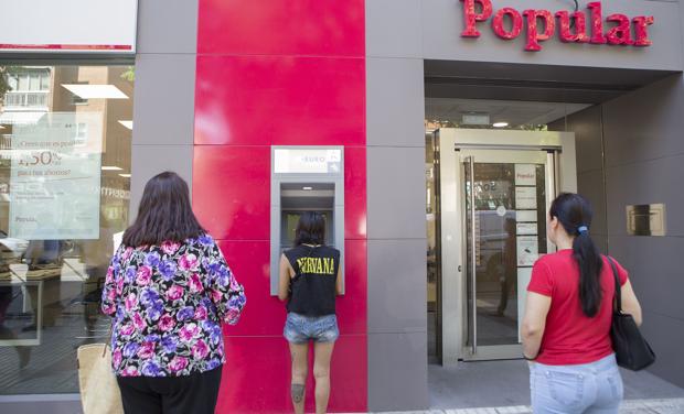 Clientes sacan dinero del cajero de una oficina del Banco Popular en Madrid.