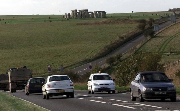 Los vehículos circulan por la carretera próxima a Stonehenge, que se recorta contra el horizonte.