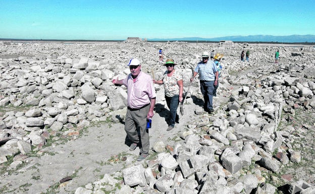 Imagen principal - Arriba. Felipe Vázquez camina seguido por Pilar Barroso y su marido, Flavio Arroyo. Las casas fueron derribadas y reducidas a piedras antes de la llegada del agua. Abajo. Izq. A flote. Imagen de Talavera la Vieja realizada con dron la semana pasada, con las aguas de Valdecañas muy bajas. Decha..