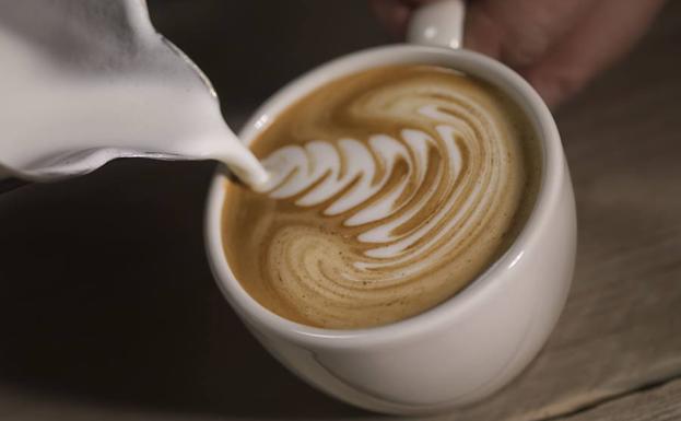 Un barista decora un café con crema de leche. 