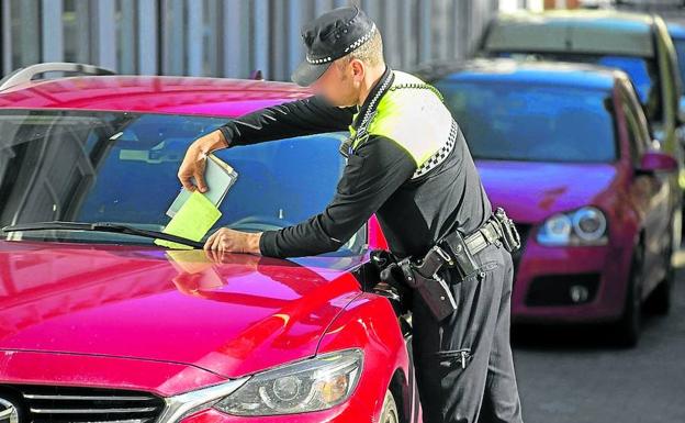 Un agente local coloca una multa en el parabrisas de un vehículo. 