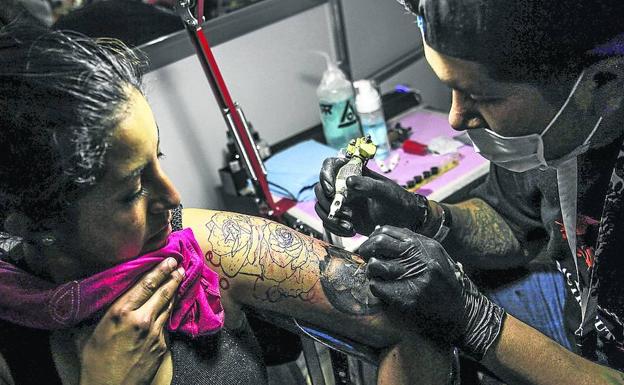 Un tatuador trabaja para ‘decorar’ el brazo izquierdo de una joven.