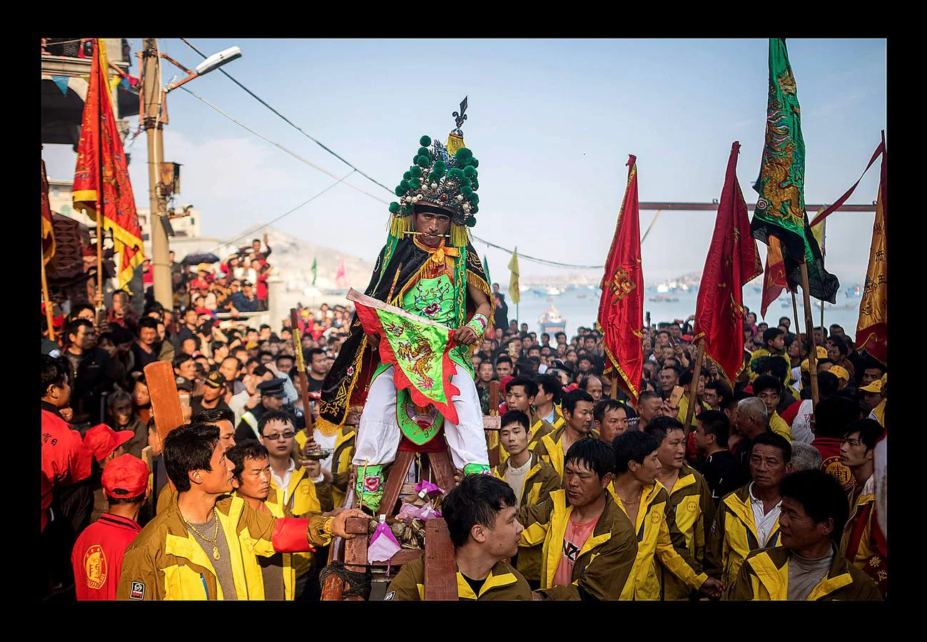 «El tablero de los dioses oceánicos» es uno de los más sorprendentes festivales que se celebran en Fuye, una localidad de la isla de Nanri, en la provincia china de Fujian. Vestidos con prendas bordadas y coronadas sus cabezas con intrincadas coberturas, una veintena de participantes cantan y blanden espadas y estandartes mientras son transportados hacia el mar en palanquines portados por convecinos. La pesca sigue siendo un trabajo arriesgado para los moradores de Fuye, que se hacen a la mar en pequeñas embarcaciones acompañados por imágenes y estatuillas para que los dioses les protejan. «Podemos pedirles que nos mantengan a salvo en el mar, pero no pueden darnos peces ni decirnos dónde hay más,» dijo Zhou, uno de tantos pescadores que estudia inglés con la esperanza de obtener trabajo en un barco de altura.