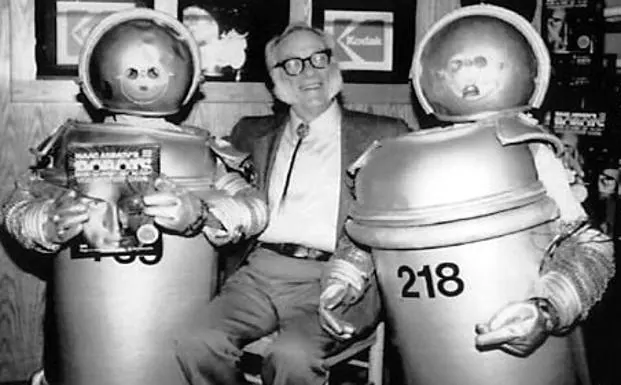 Isaac Asimov posa con dos objetos que simulan ser robots. 