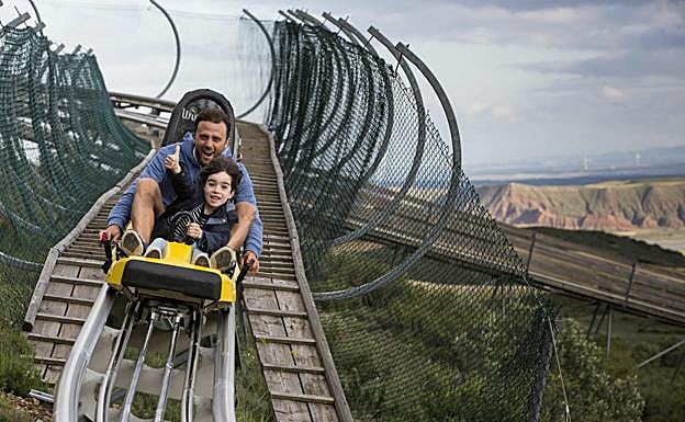 Un adulto y un niño se deslizan por la pista de bobsleigh que atraviesa el parque.