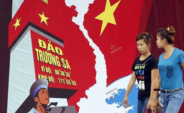 Dos mujeres pasan ante un mural alusivo al conflicto fronterizo entre China y Vietnam en Hanoi. Abajo, la polémica prenda de GAP.