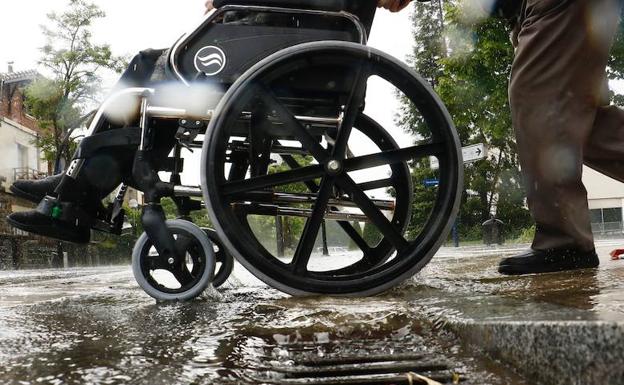 Un hombre empuja una silla de ruedas bajo la lluvia.