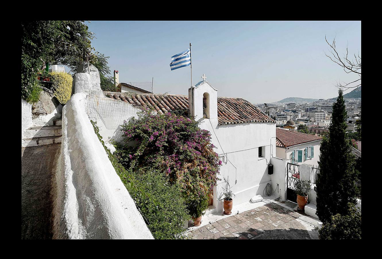 El distrito de Anafiotika, en Atenas, tiene el aire de un pintoresco pueblo de piedra sacado de las islas Cícladas, pero se encuentra a los pies de la Acrópolis. Quien ascienda por las estrechas y sinuosas calles del distrito de Plaka se sorprenderá ante la vista de un pueblo casi idéntico a los de las islas del mar Egeo. De hecho, las cien casas con techos de tejas, conocidas como Anafiotika, son tan antiguas como la capital griega moderna. Y es que para devolver a la ciudad su gloria clásica tras la guerra contra el imperio Otomano, el rey de Grecia invitó a los mejores canteros de la isla egea de Anafi a trabajar en su reconstrucción.