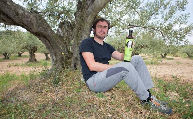 Juan Luis Bujanda sostiene una botella de aceite en un olivar.