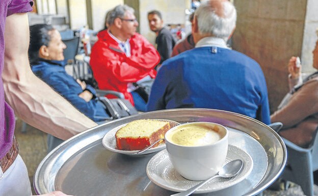 Un camarero sirve un café con leche y un bizcocho en la terraza de un local de la plaza de España.