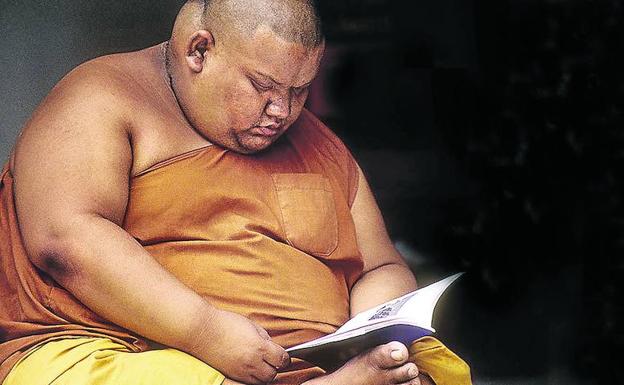 Un monje tailandés con evidente sobrepeso se dedica a la meditación a través de la lectura.