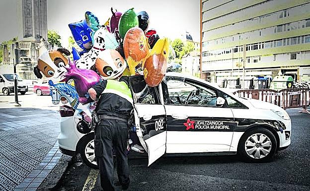 Un policía municipal mete en un coche patrulla unos globos incautados a un hombre que había sido denunciado por varios vendedores legales.