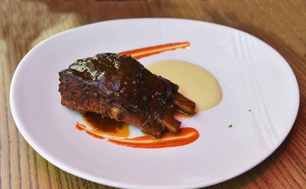 La costilla asada de cerdo gallego, criado con castañas, acompañada de cremoso de patata y salsa barbacoa vizcaína.